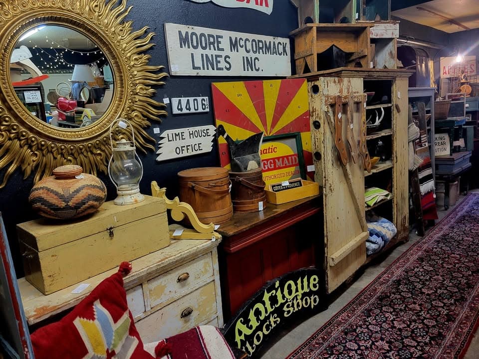 A carved gold sunburst mirror glowing on a dark wall at M & M, above vintage signage and stoneware